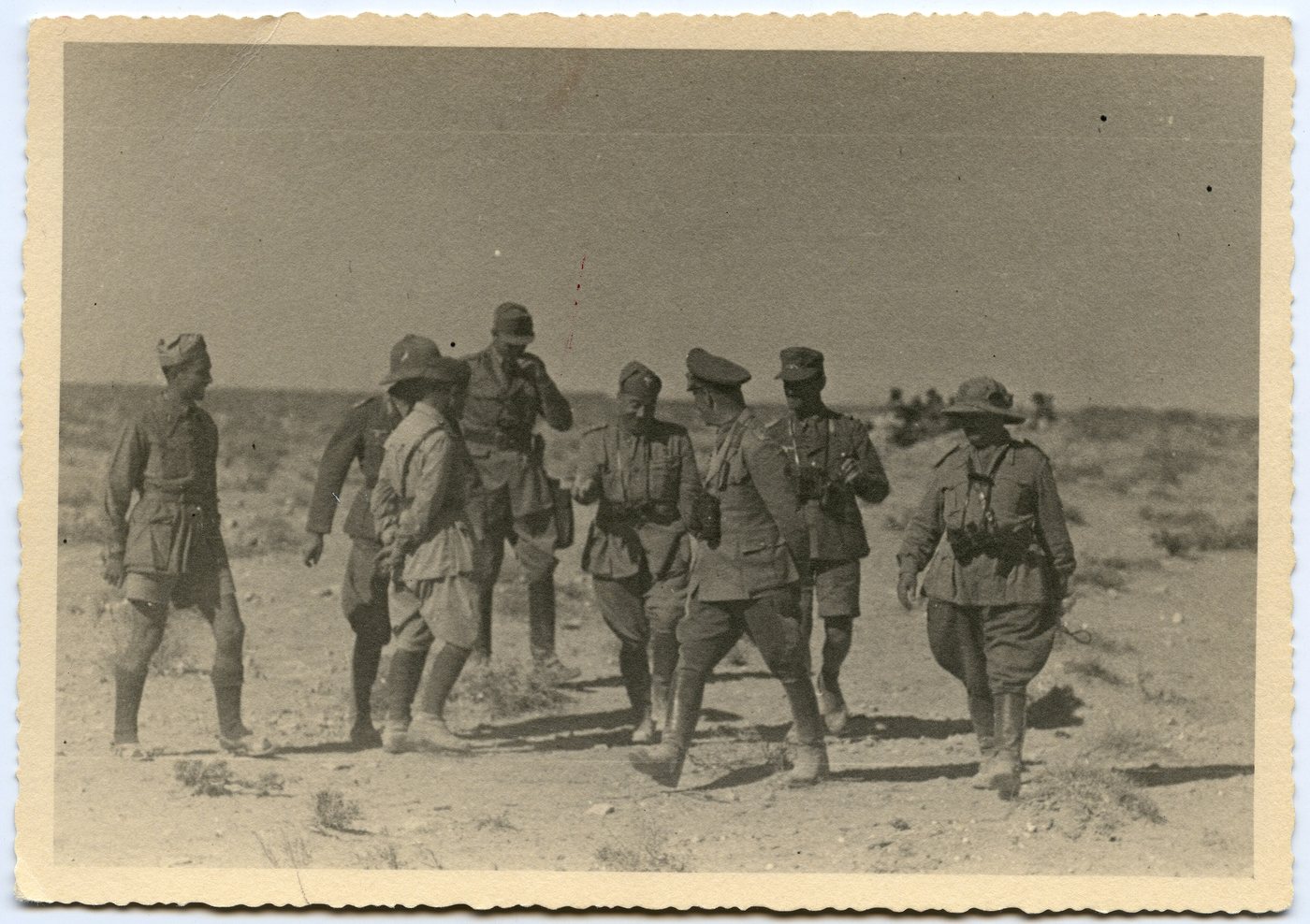 Old sepia snapshot of a group of officers in tropical uniforms walking across stony desert