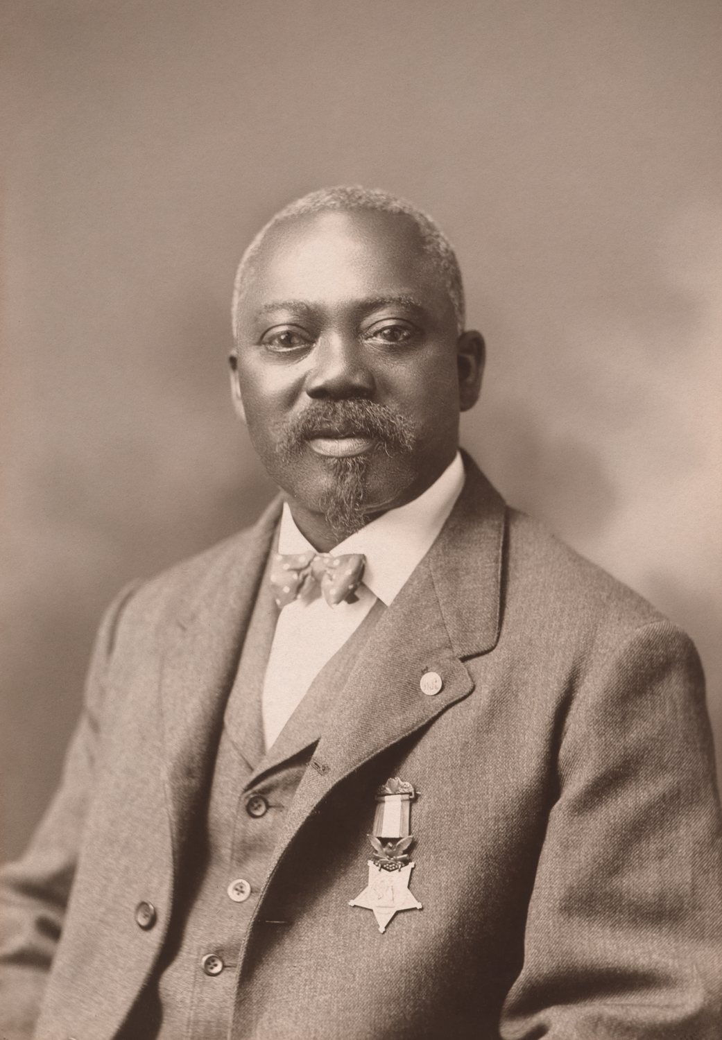 Sepia photograph of a grey-bearded Black man in a suit with a medal pinned to his chest