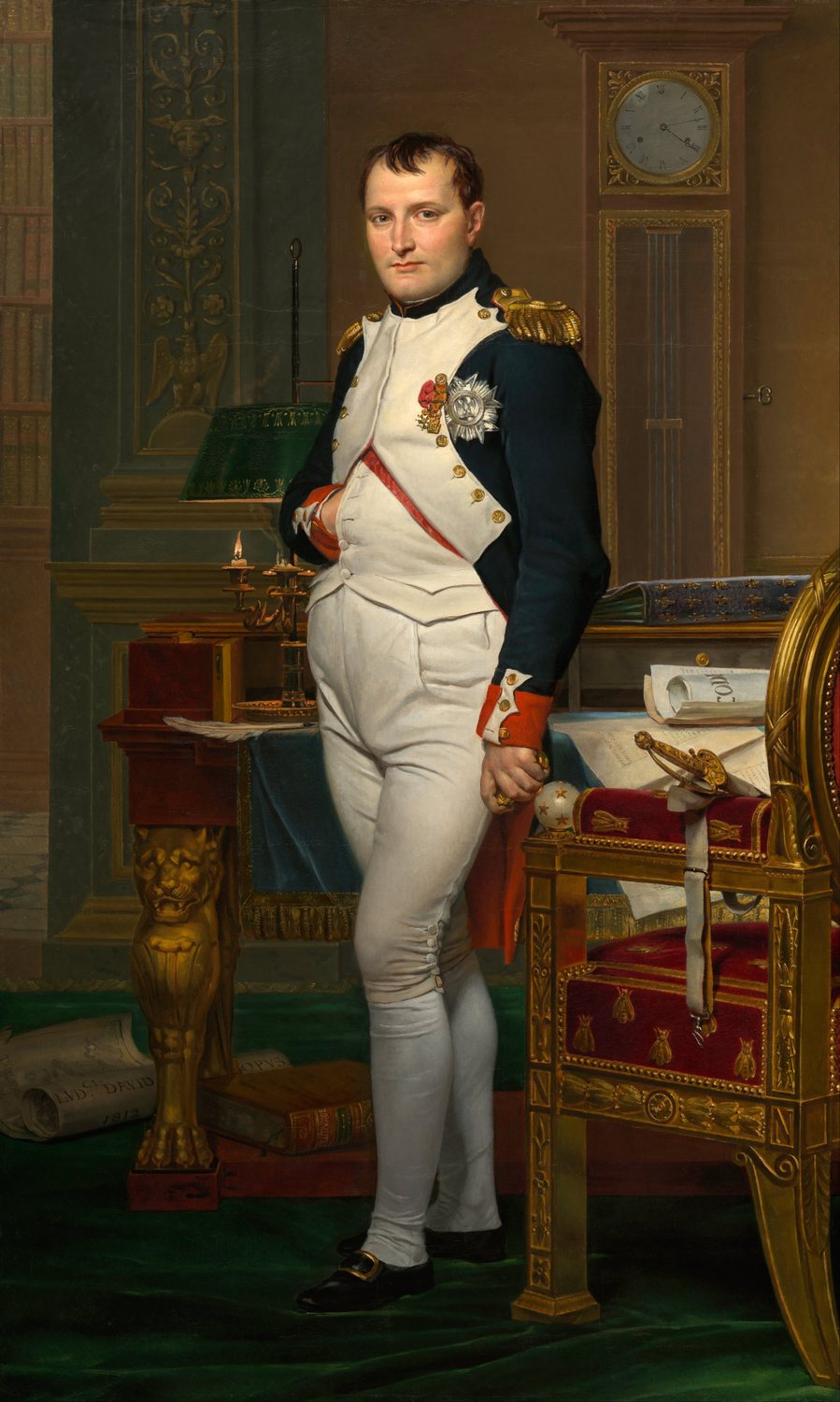 Full-length painting of Napoleon standing in uniform with a hand in his waistcoat beside a desk