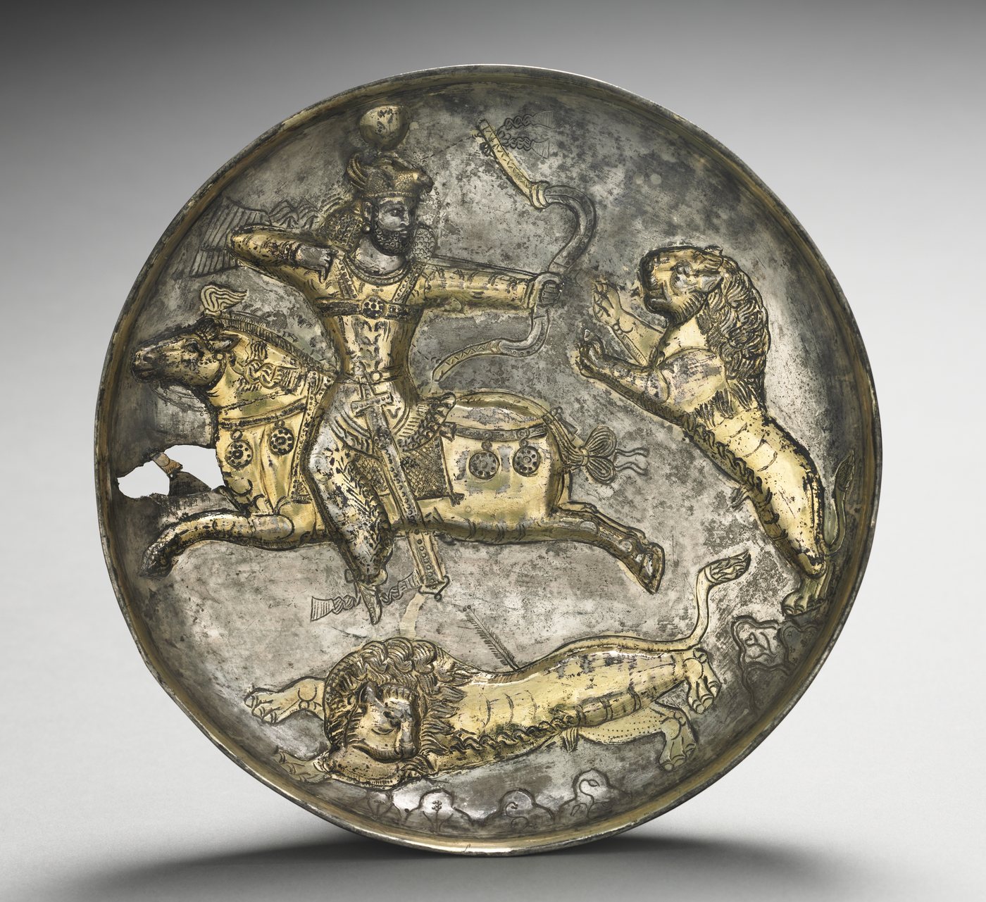 Silver dish with a mounted king shooting backwards at a lion