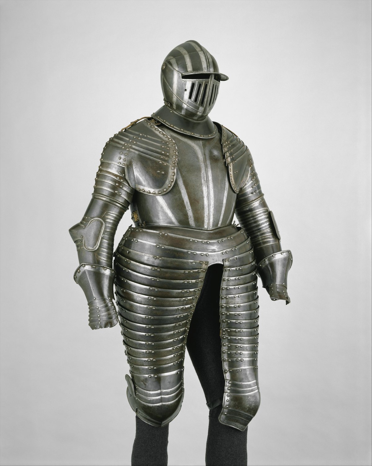A full cuirassier armor of dark steel with a closed helmet, articulated shoulder and arm plates and long lames covering the thighs to the knee