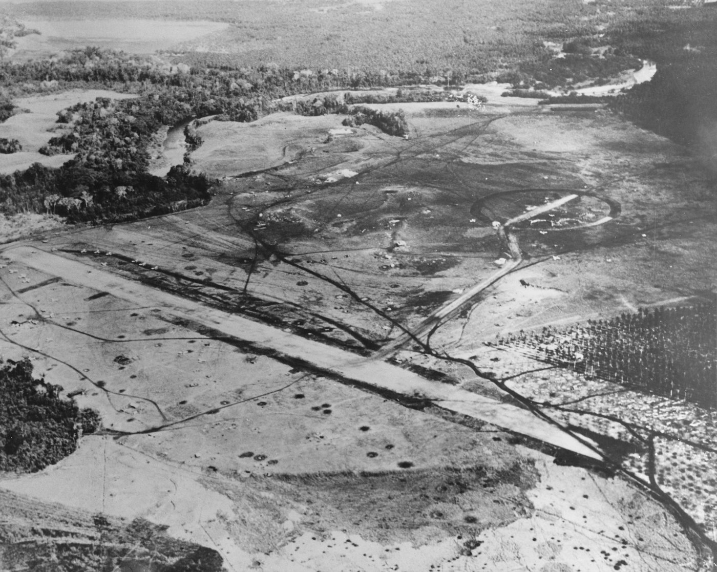 Black and white aerial photograph of an airstrip cut through jungle and grassland