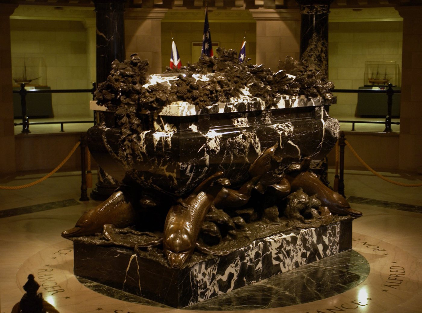 Photograph of a marble sarcophagus in a crypt with a midshipman standing guard