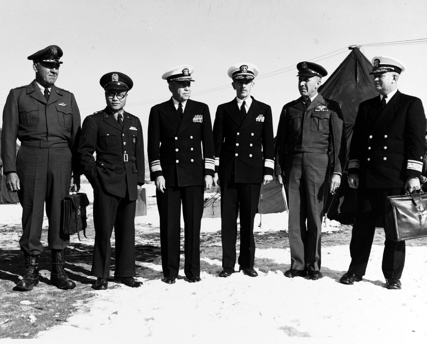 Black and white photograph of six officers in uniform standing in a row on snowy ground in front of tents: two US Navy admirals in dark coats in the center, a South Korean general in glasses on the left.