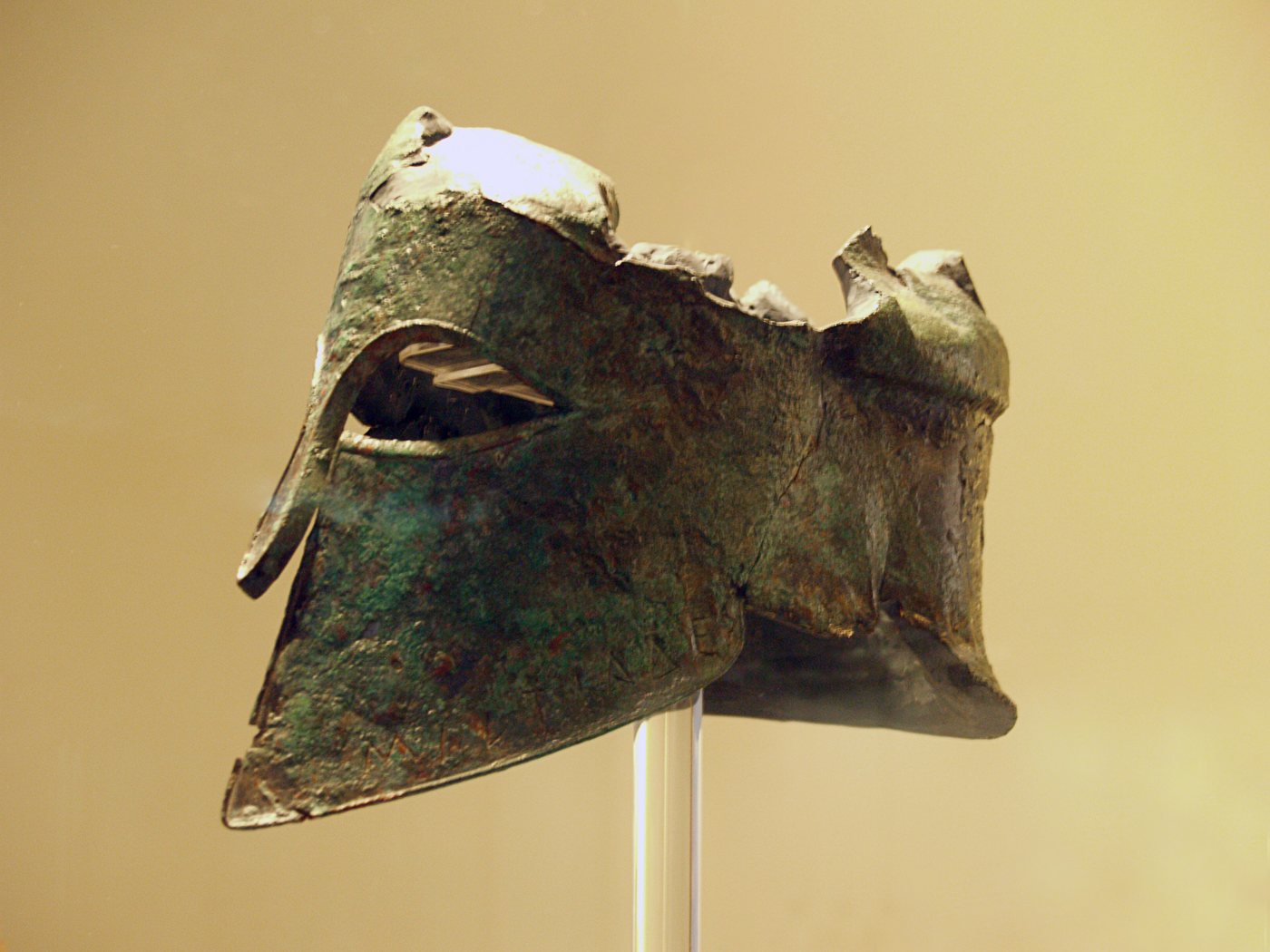 Corroded bronze Corinthian helmet on a museum stand
