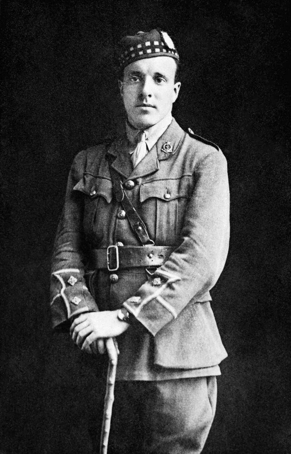Portret studyjny Noela Chavasse'a w mundurze oficerskim i szkockiej czapce, wspartego na lasce
