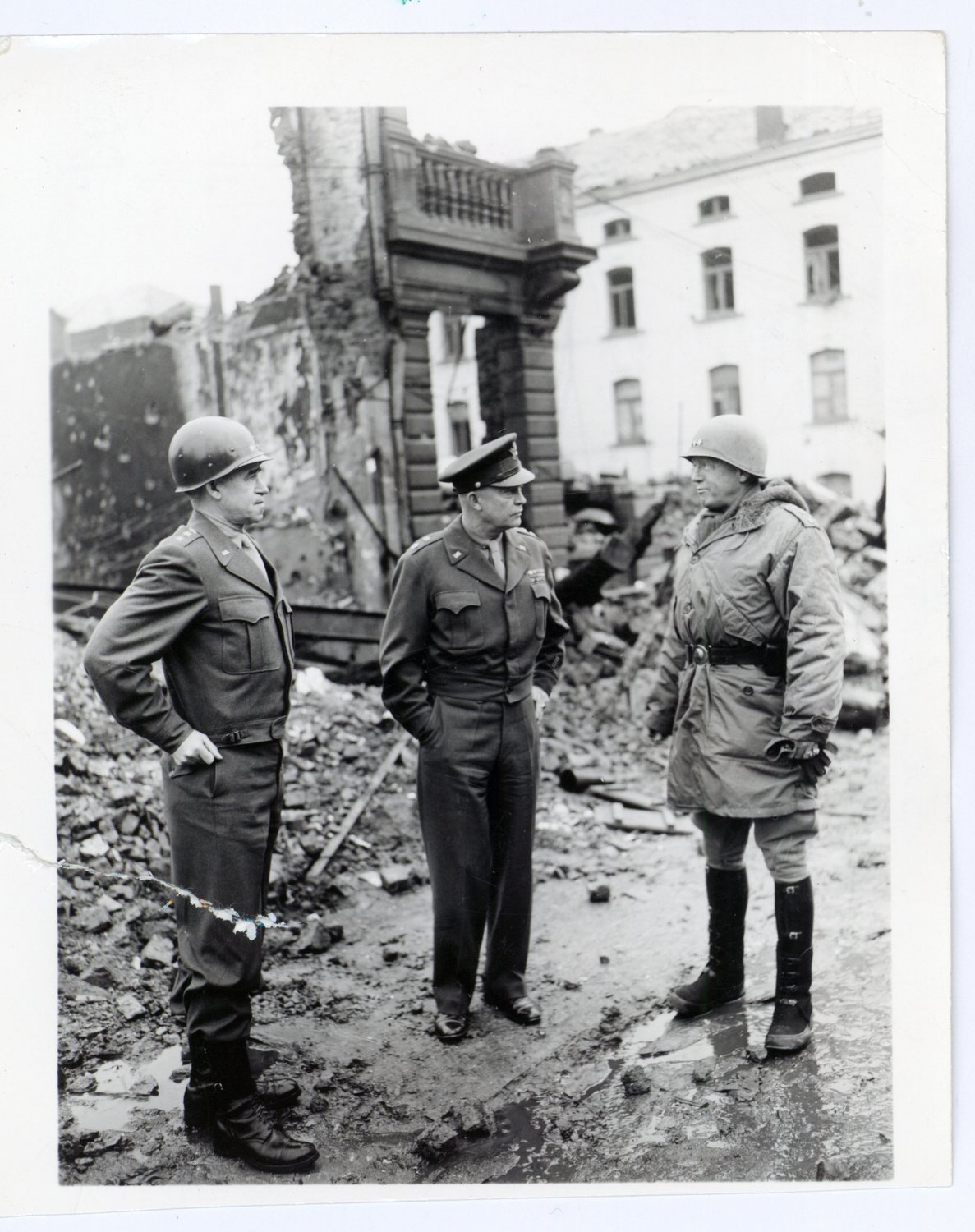 Black-and-white photo of three American generals in uniform standing among ruined buildings