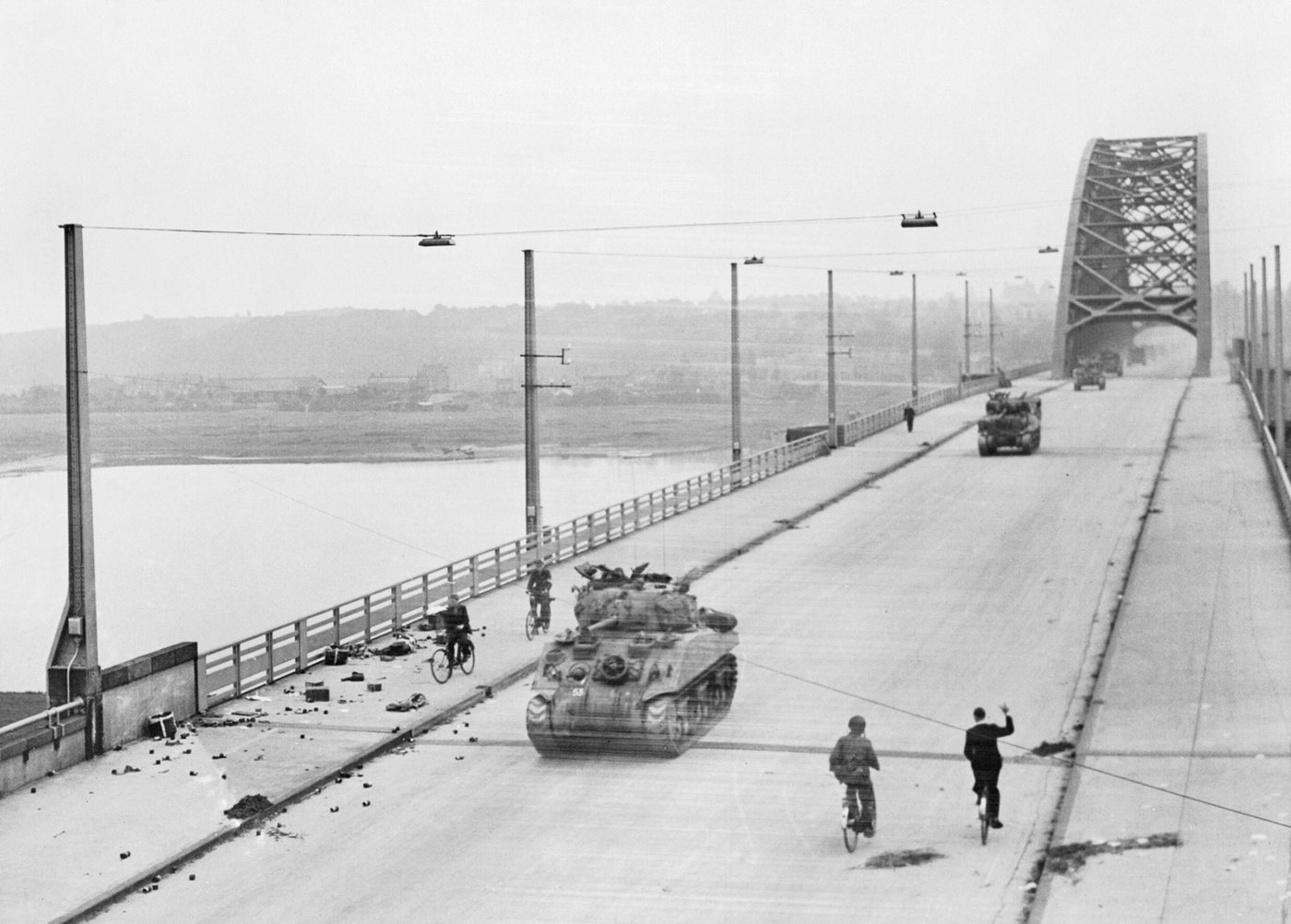 A Sherman tank crossing the long steel arch road bridge at Nijmegen, with soldiers and cyclists on the roadway