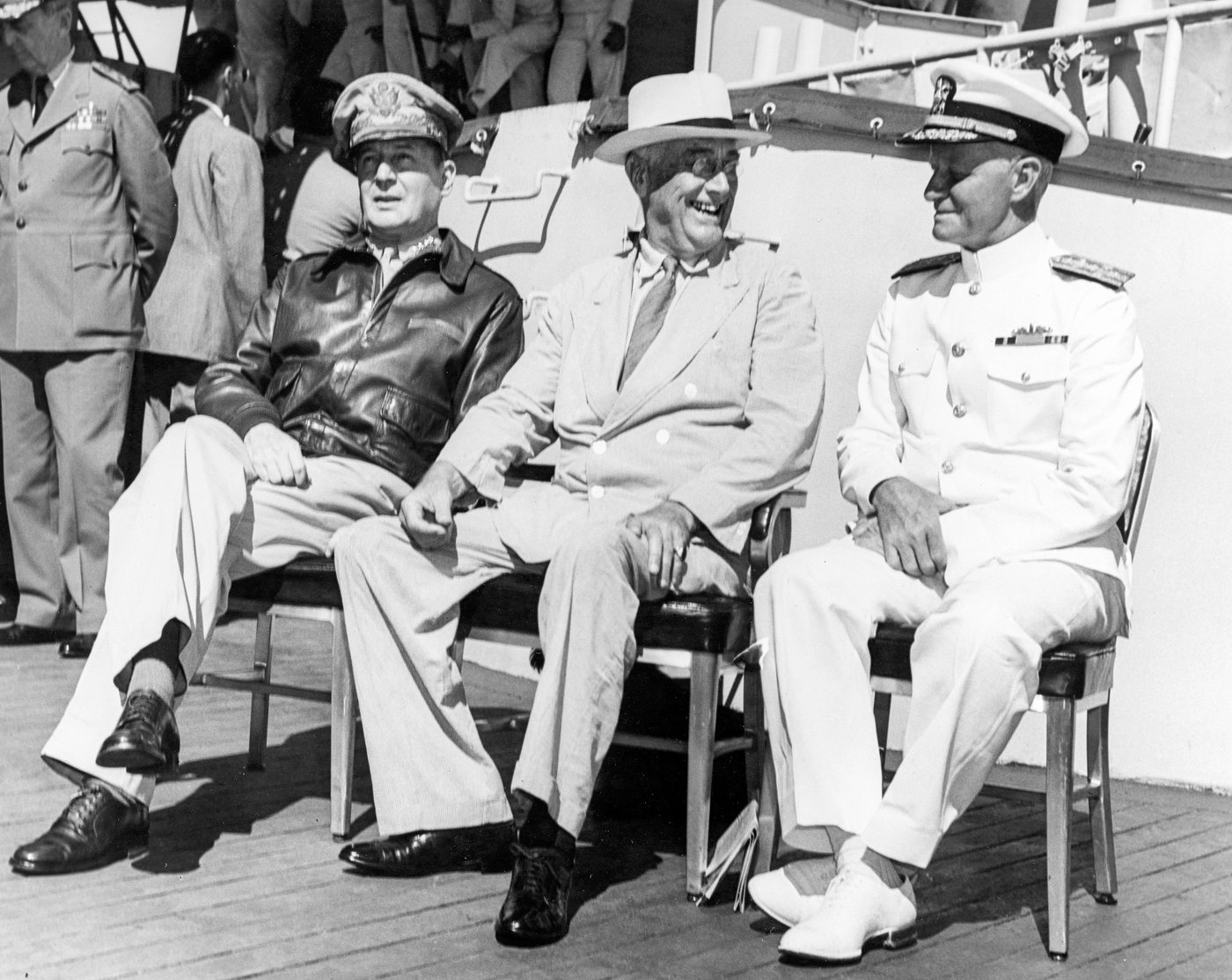 Black and white photograph of MacArthur, Roosevelt and Nimitz seated side by side on a ship's deck