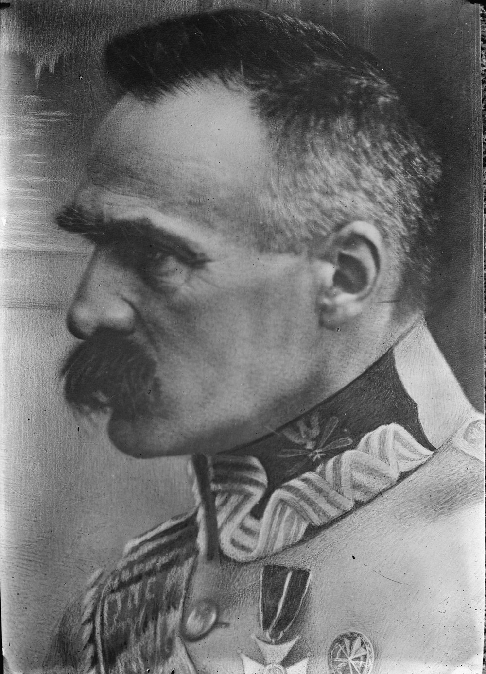 Czarno-biały portret Józefa Piłsudskiego z profilu, z sumiastymi wąsami, w mundurze z haftowanym kołnierzem i odznaczeniami.