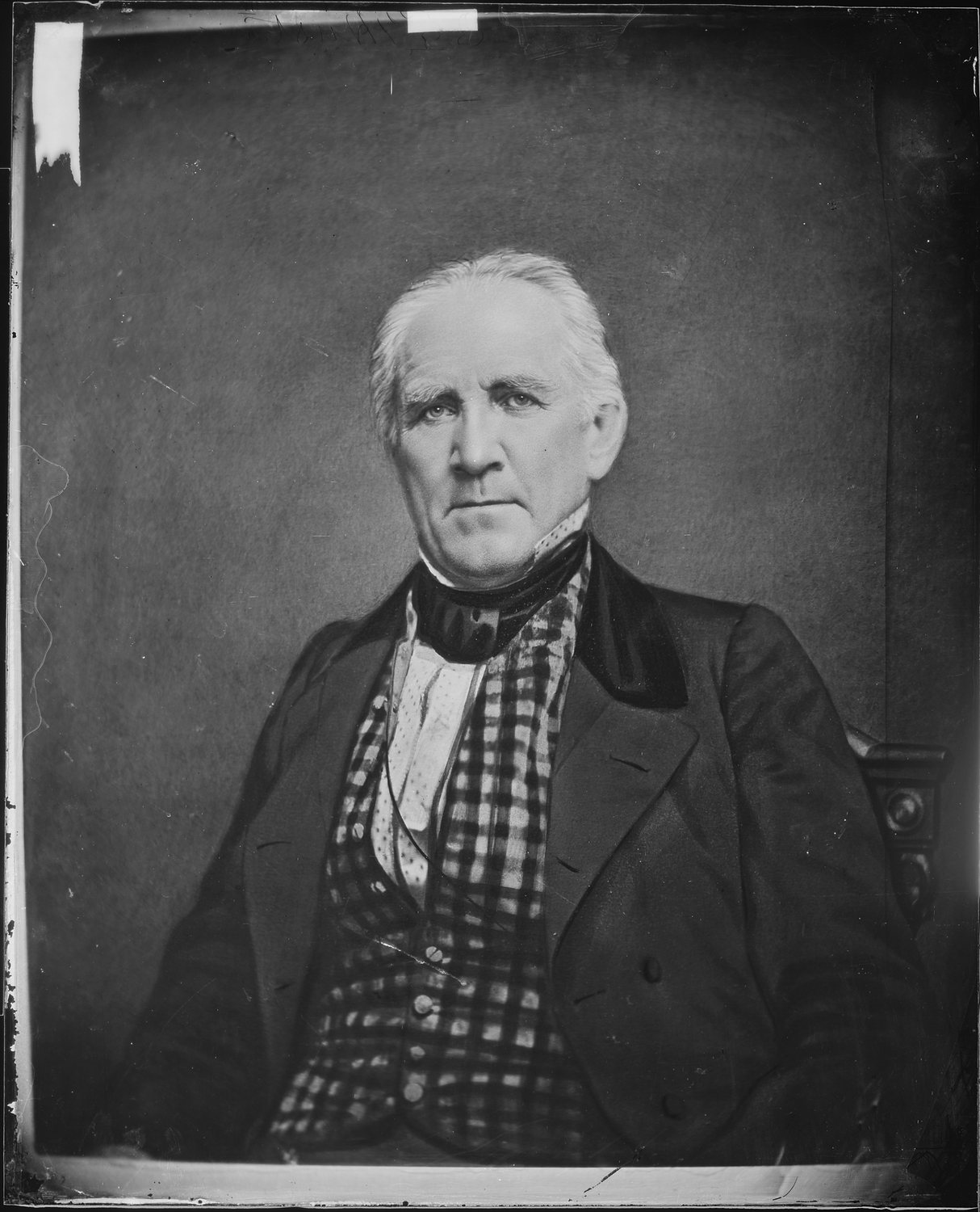 Black and white photograph of an elderly white-haired man in a dark coat and checked waistcoat