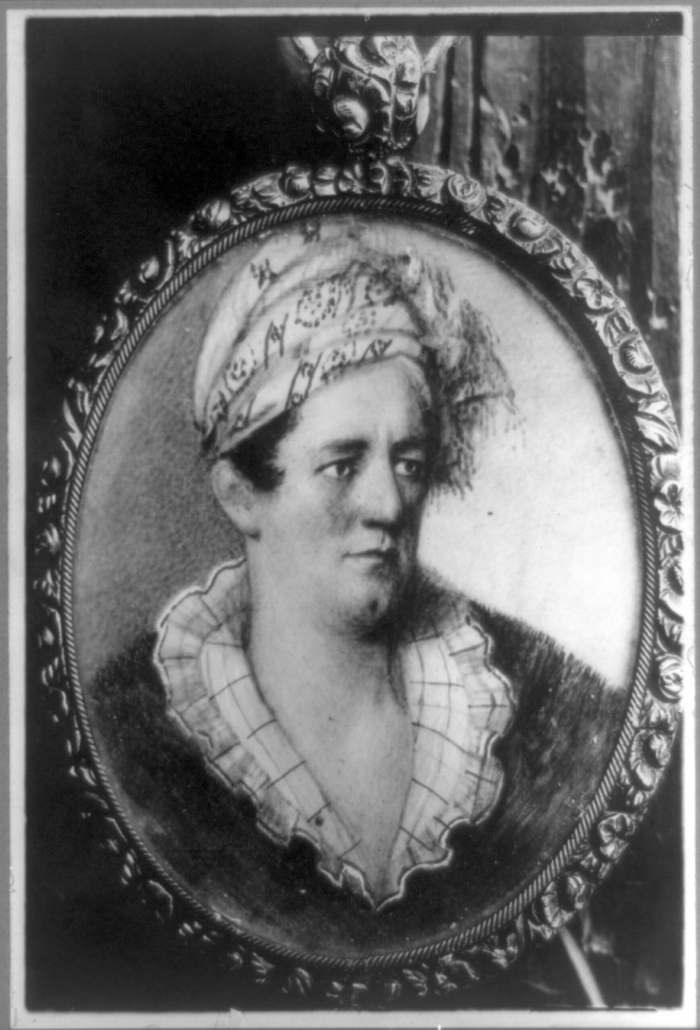 Black and white oval portrait of a man wearing a turban and a ruffled shirt