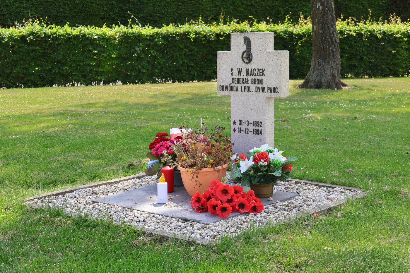 White stone cross marking General Maczek's grave, with flowers and candles in front