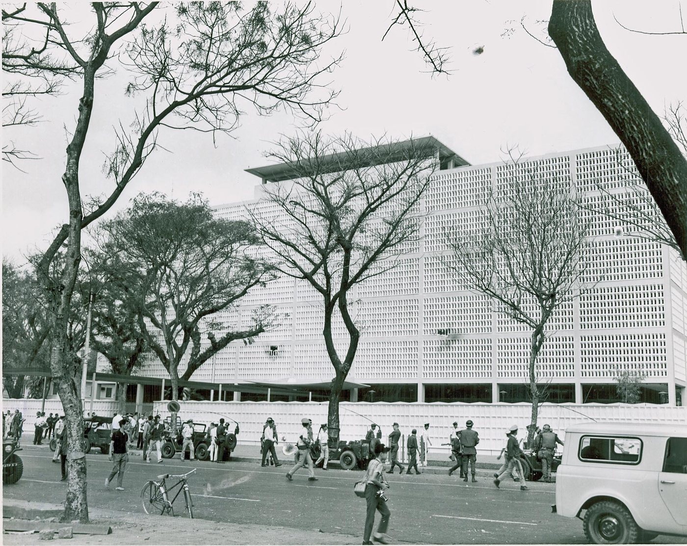 Black and white photograph of the US embassy building in Saigon behind its wall, with people in the street