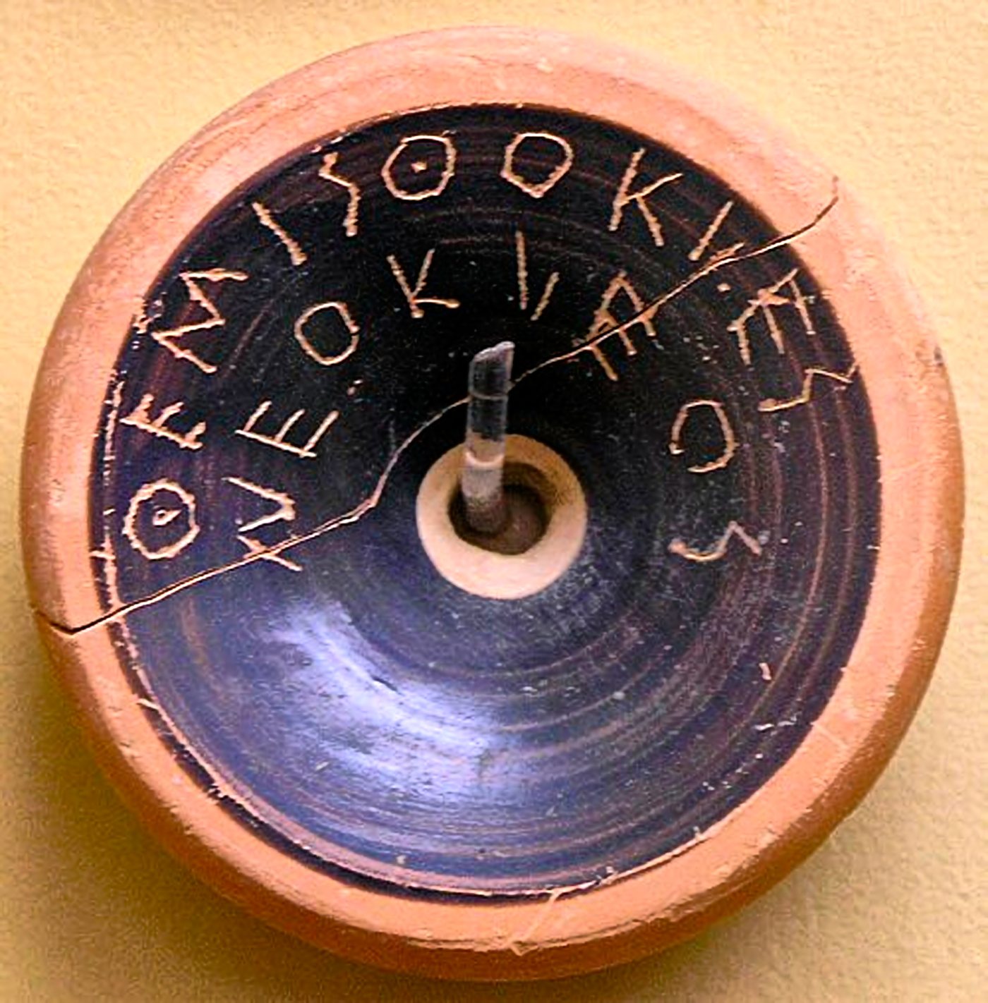 Round pottery fragment with Greek letters scratched in a spiral
