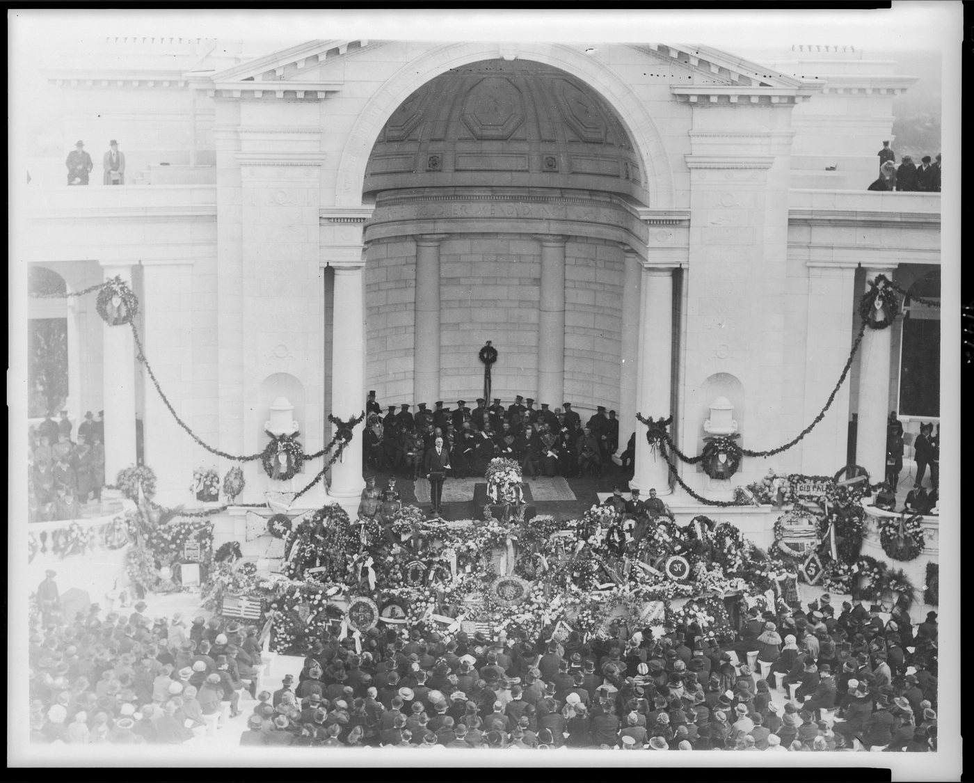 Crowds and wreaths around a speaker in front of the Arlington amphitheater in 1921