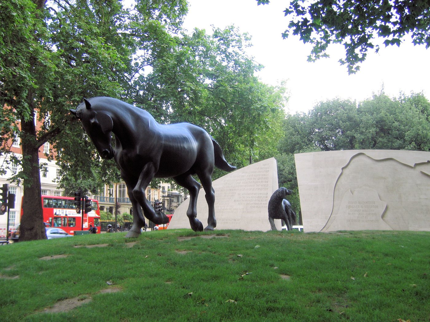 Bronze statues of a horse and a dog on a grass mound beside a carved stone wall in London