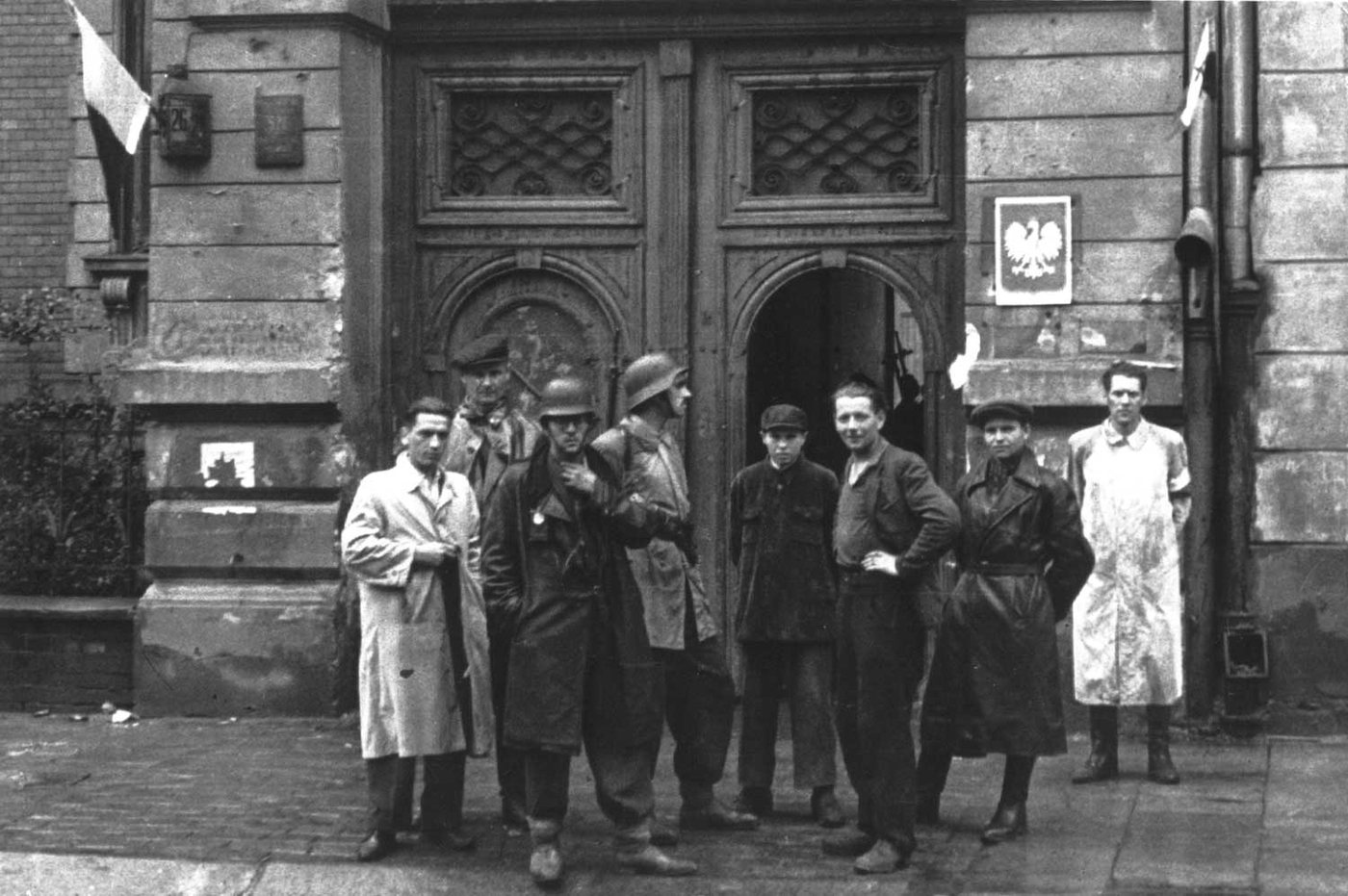Black and white photograph of a group of armed men in coats and armbands outside a building