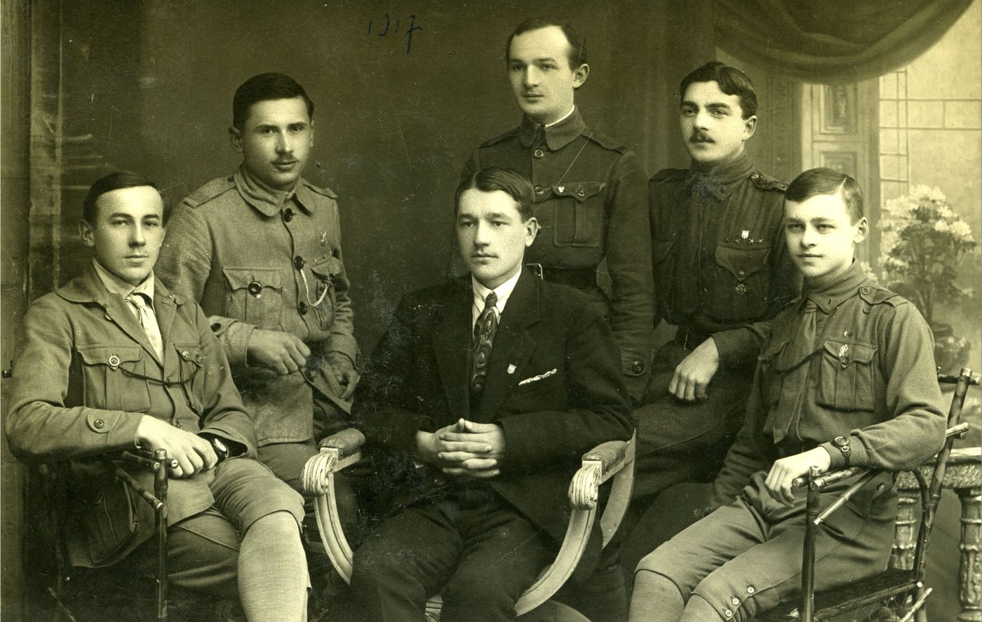 Studio group photograph of six young men in uniforms and suits, two seated in front