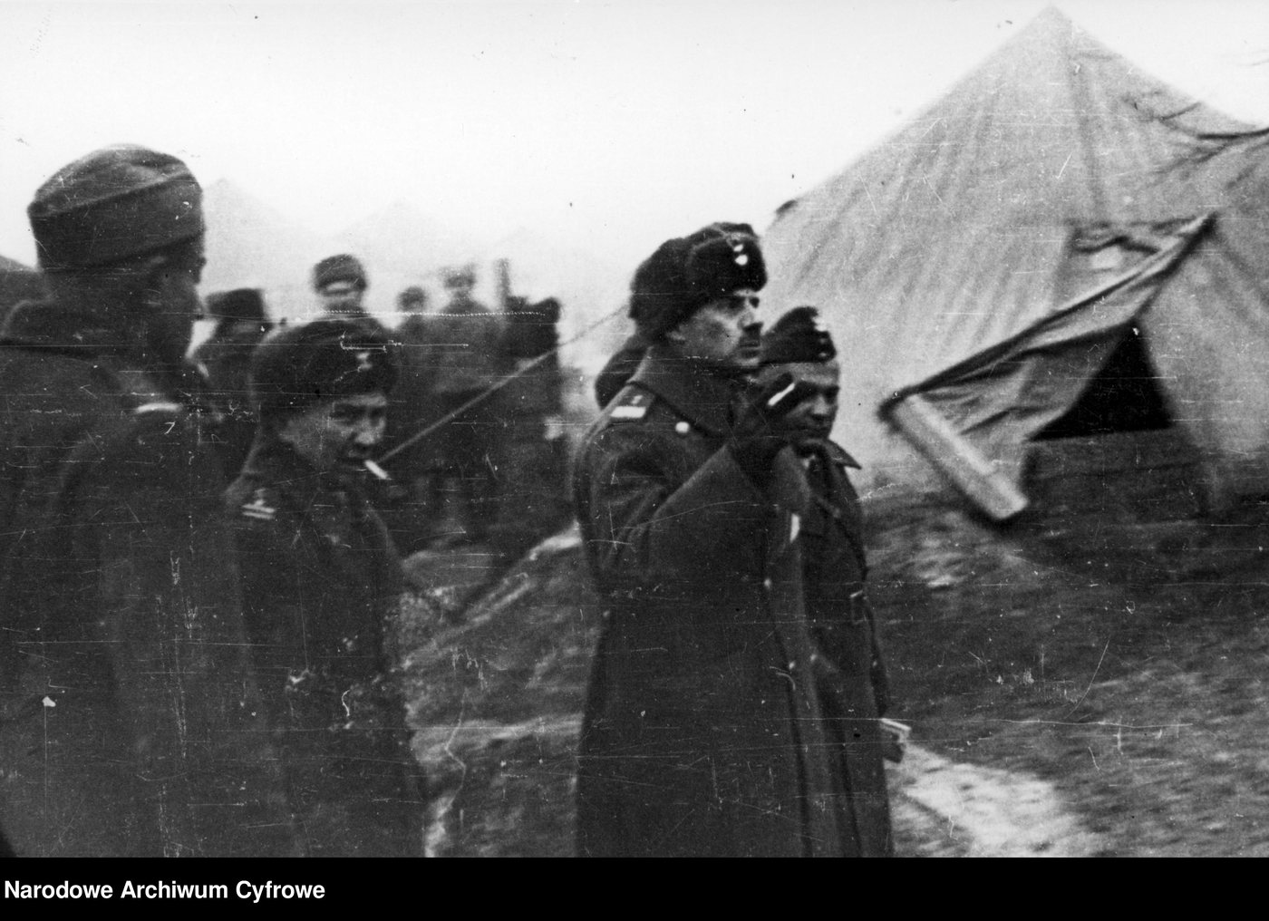 Officers in winter coats and fur caps standing among tents in a Polish army camp in the USSR