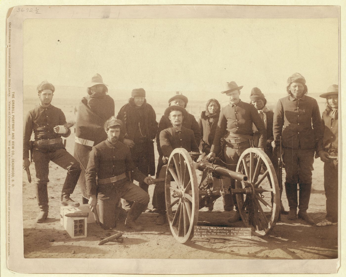 Soldiers and Lakota scouts in winter clothing posed behind a small wheeled Hotchkiss gun
