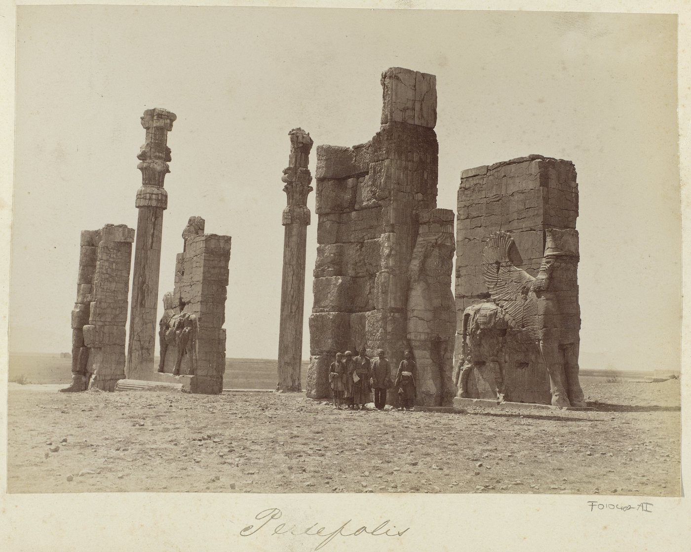 19th-century photograph of the ruined stone gateway of Persepolis with columns and a group of men at its foot